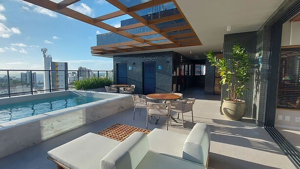 A rooftop pool area with a glass balustrade, lounge chairs, and a seating area with a table and chairs.
