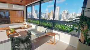 A modern living room with a city view, featuring a sofa, a dining table, and a green chair.