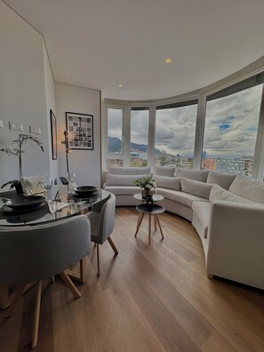 A modern living room with a dining area, large windows with a city view, and a curved sofa. - VOU by Wellcome (Bogotá)