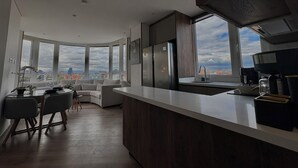 A modern kitchen with a large window, a dining area with a round table, and a view of the cityscape. - VOU by Wellcome (Bogotá)