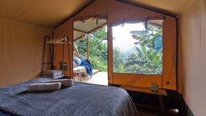 Une pièce aménagée comme une tente, avec un lit, un fauteuil suspendu et une vue sur la verdure environnante.