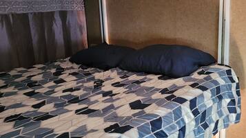 A bed with a patterned bedspread, a dark pillow, and a suitcase under the bed.
