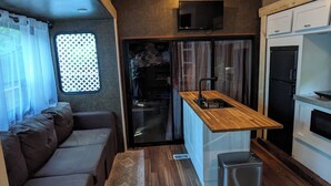 A compact RV interior with a kitchenette, a seating area, and a small dining table. - 2-bedroom RV in beautiful Bowser with WiFi, AC (Bowser)