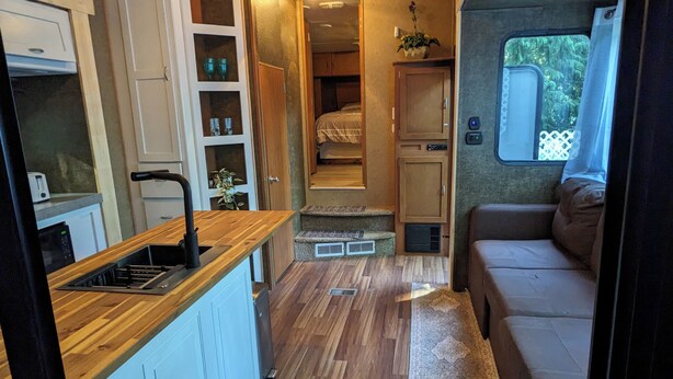 A compact RV interior with a kitchenette, a small bathroom, and a seating area. - 2-bedroom RV in beautiful Bowser with WiFi, AC (Bowser)