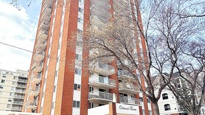 A multi-story residential building with a brick facade, multiple balconies, and a sign indicating the name 'Oakwood Towers.' - Downtown Condo near Rogers | Parking, Pool, Gym (Edmonton)