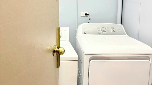 A laundry room with a white washing machine, a door with a brass handle, and a sign that reads 'LAUNDRY ROOM'. - Downtown Condo near Rogers | Parking, Pool, Gym (Edmonton)