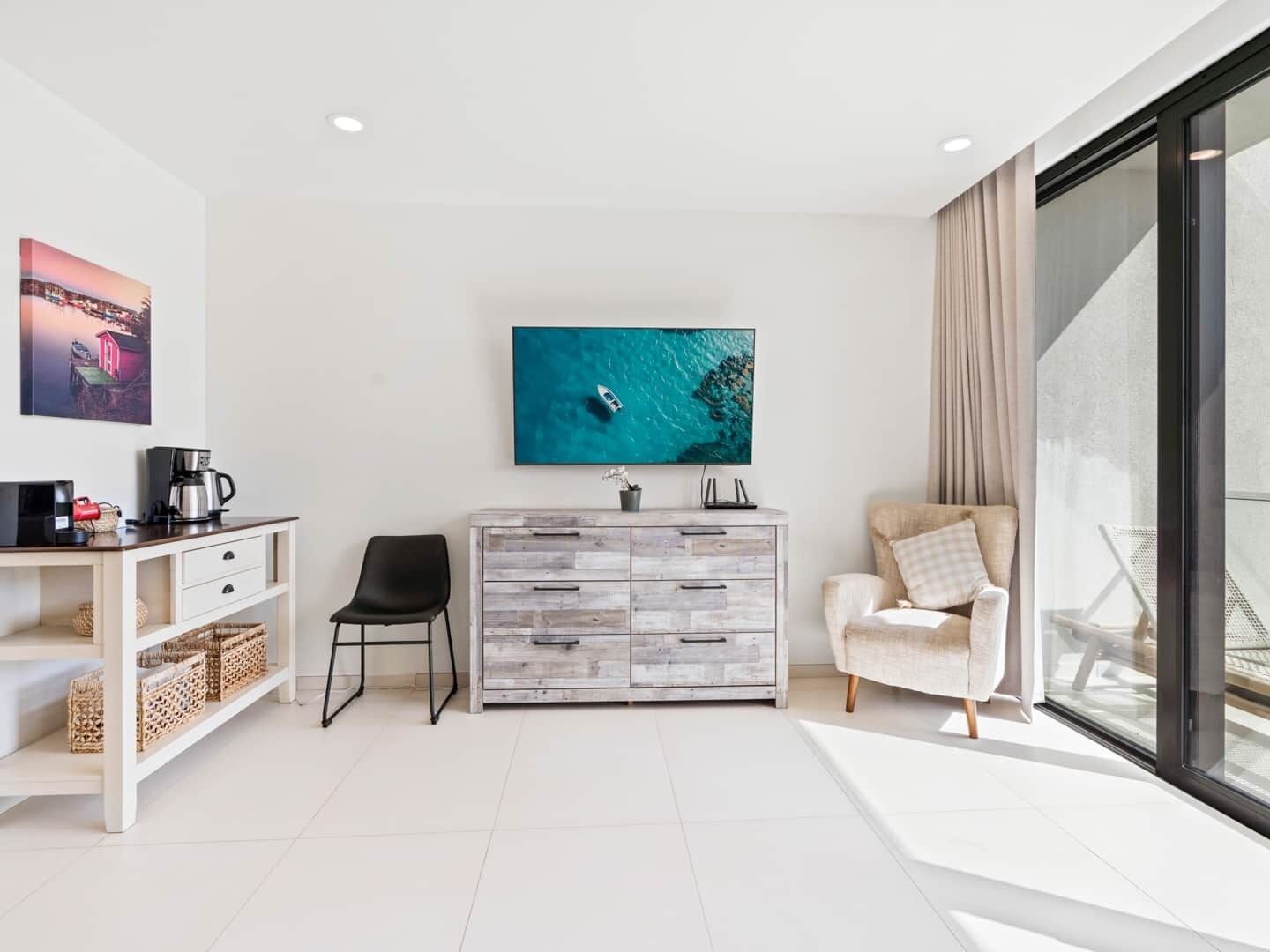 Un soggiorno moderno con un divano bianco, una poltrona nera, un mobiletto in legno e un grande televisore che mostra una scena di mare azzurro.