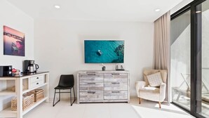 Een moderne woonkamer met een witte bank, een zwarte fauteuil, een houten kast en een grote televisie waarop een blauw zeegezicht te zien is.