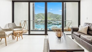 Een moderne woonkamer met een grote schuifdeur die leidt naar een balkon met uitzicht op een jachthaven en heuvels.