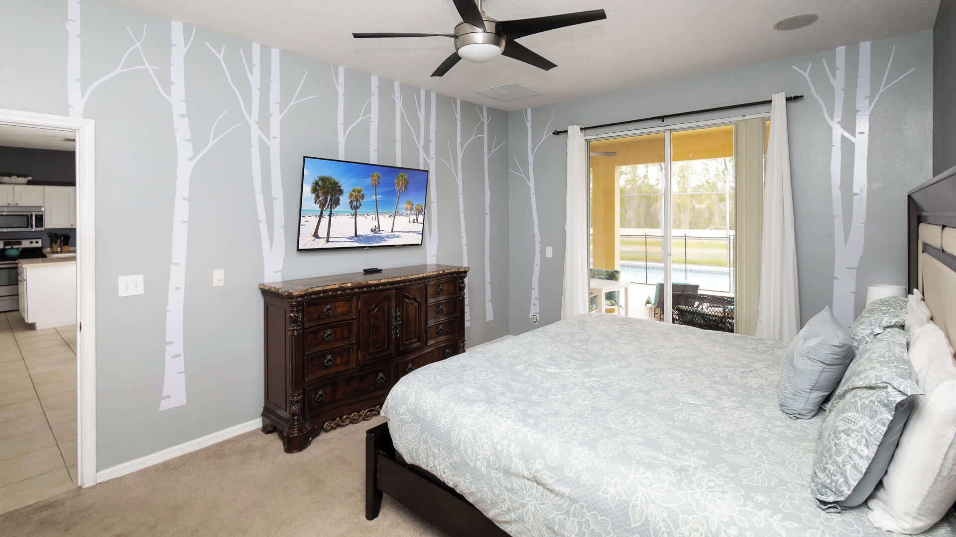 Ein Schlafzimmer mit einem großen Bett, einem Fernseher an der Wand und Blick ins Freie durch eine Schiebetür.