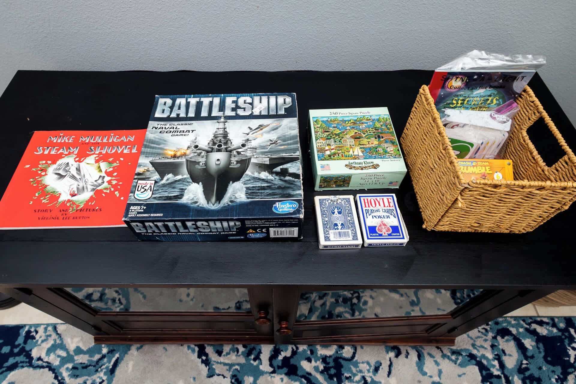 A table with various board games and books, including Battleship, a 250-piece jigsaw puzzle, and a Scrabble set.