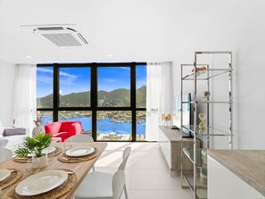 A modern dining area with a view of a coastal landscape, a red chair, and a glass shelf unit. - C355 - Top Floor with Lagoon View (Cole Bay)