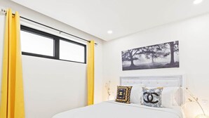 A bedroom with a bed, curtains, a nightstand, a lamp, and a wall-mounted picture.