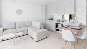 A modern living room with a sofa, ottoman, and coffee table, a dining area with chairs and a table, and a kitchen with appliances and cabinets. - C304 – 1 bedroom apartment with terrace (Sint Maarten)
