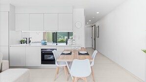 A modern kitchen with white cabinetry, a built-in oven, and a dining area with a wooden table and white chairs. - C304 – 1 bedroom apartment with terrace (Sint Maarten)