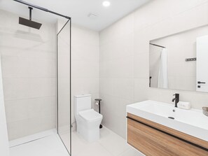 Un baño moderno con ducha de vidrio, inodoro blanco y tocador con espejo.