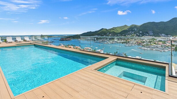Ein Pool auf dem Dach mit klarem, blauem Wasser, einer Holzterrasse und Blick auf eine Marina und Berge.