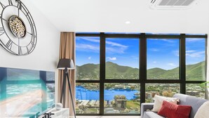 Uma sala de estar moderna com uma televisão grande, um sofá, uma mesa de centro e vista para um corpo de água e colinas.