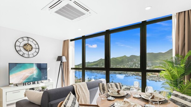 Sala de estar moderna com uma janela ampla que oferece uma vista panorâmica de uma baía e montanhas.