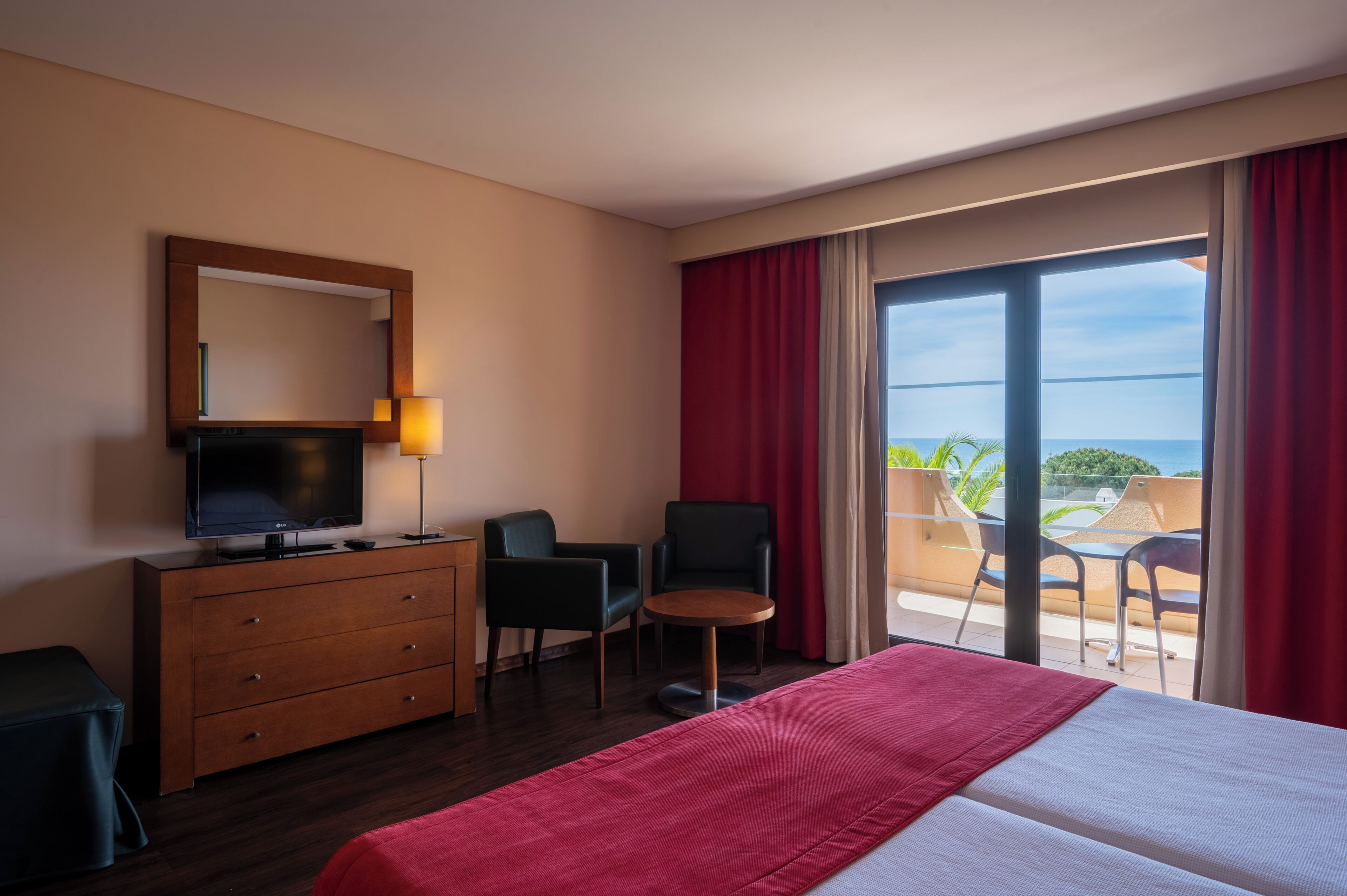 Ein Hotelzimmer mit Bett, Fernseher, Kommode, Stuhl und einem Balkon mit Blick.