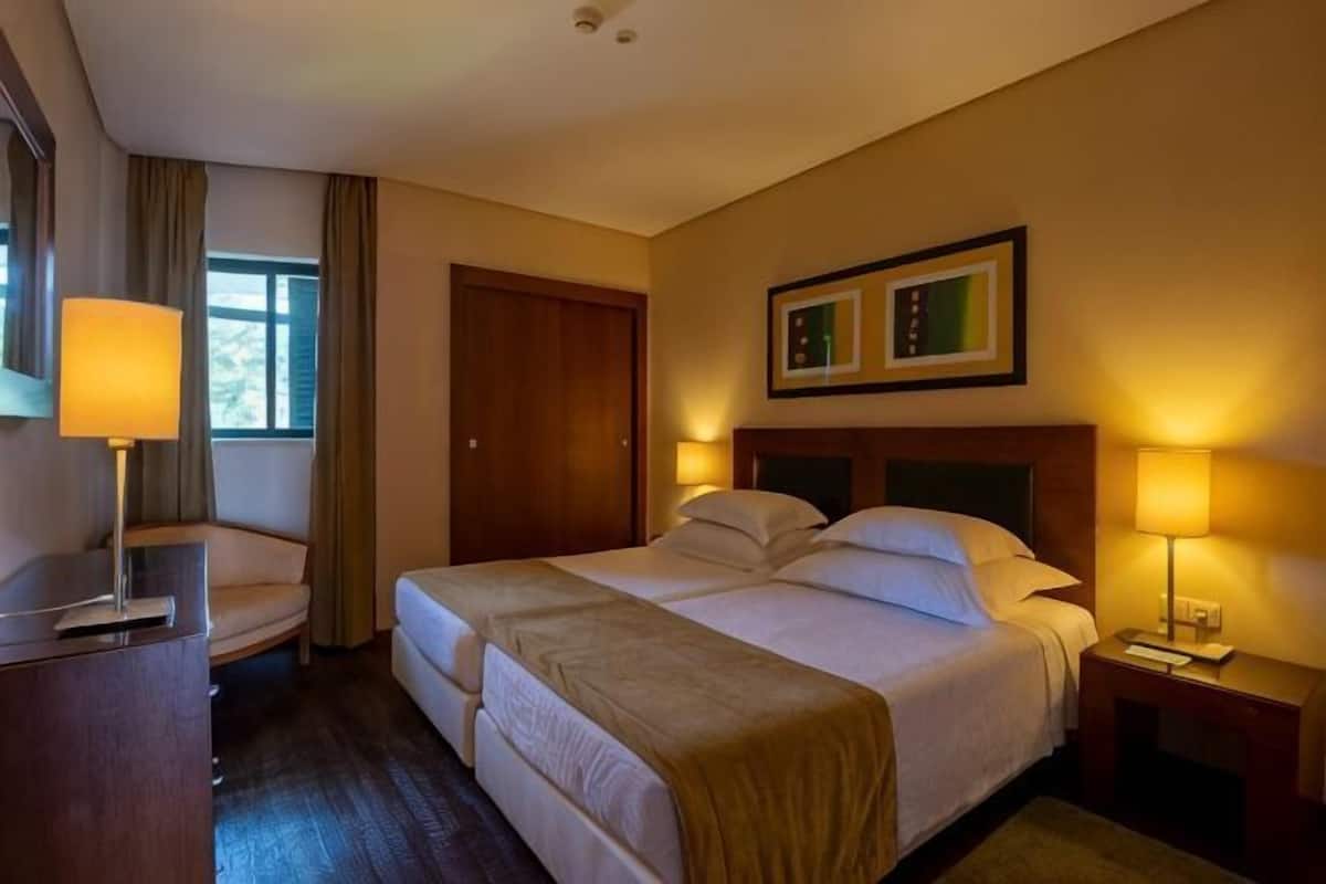 Habitación de hotel con cama doble, mesitas de noche, escritorio, silla, puerta y ventana.