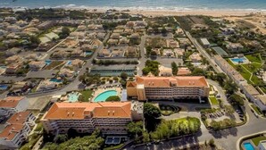 Eine Vogelperspektive auf ein Küstenresort mit mehreren Gebäuden, einem zentralen Schwimmbecken und einem Strand im Hintergrund.