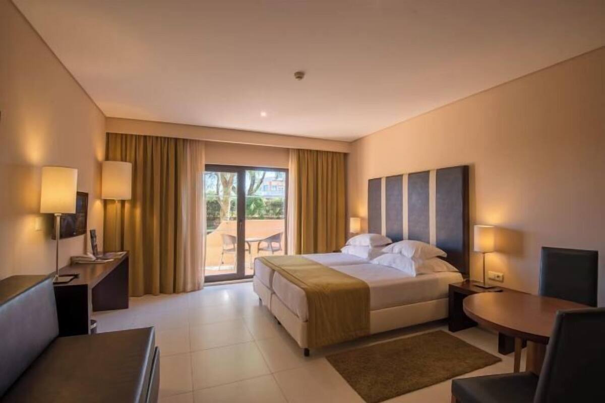 Habitación de hotel con cama, escritorio, silla, mesa y vista a través de un ventanal.