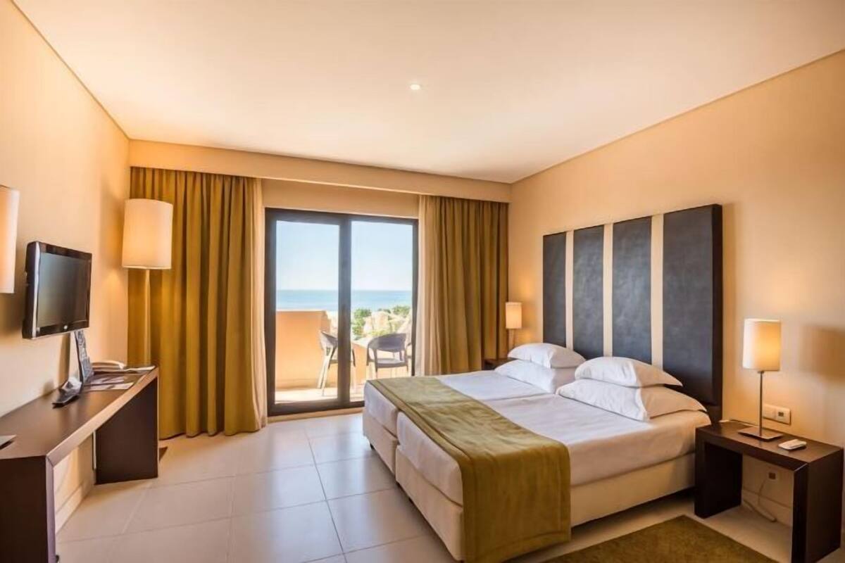 Habitación de hotel con cama, escritorio, televisor, silla y vistas al exterior.