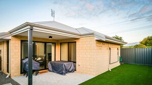 Ein modernes Haus mit überdachter Terrasse, Rasenfläche und umzäunter Garten.