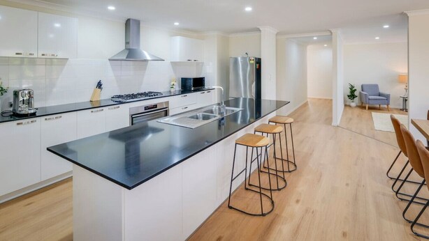 Een moderne keuken met een centraal eiland, witte kasten, roestvrijstalen apparatuur en een zithoek met krukken.