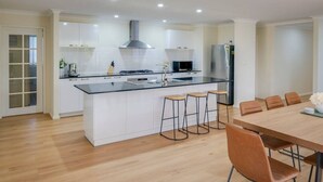 Een moderne keuken met een centraal eiland, barkrukken en een eethoek met een tafel en stoelen.