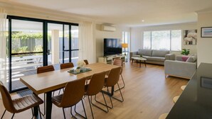 Een moderne woonkamer met een eethoek, een grijze bank en een televisie.