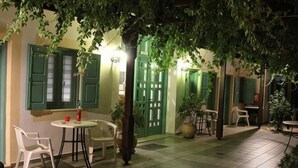 An outdoor patio area with a table and chairs, a potted plant, and a door with green shutters. - Matala Dimitris Resort (Matala)