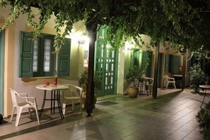 An outdoor patio area with a table and chairs, a potted plant, and a door with green shutters. - Matala Dimitris Resort (Matala)