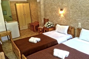 A room with two beds, a desk, a chair, a small table, and a refrigerator. - Matala Dimitris Resort (Matala)