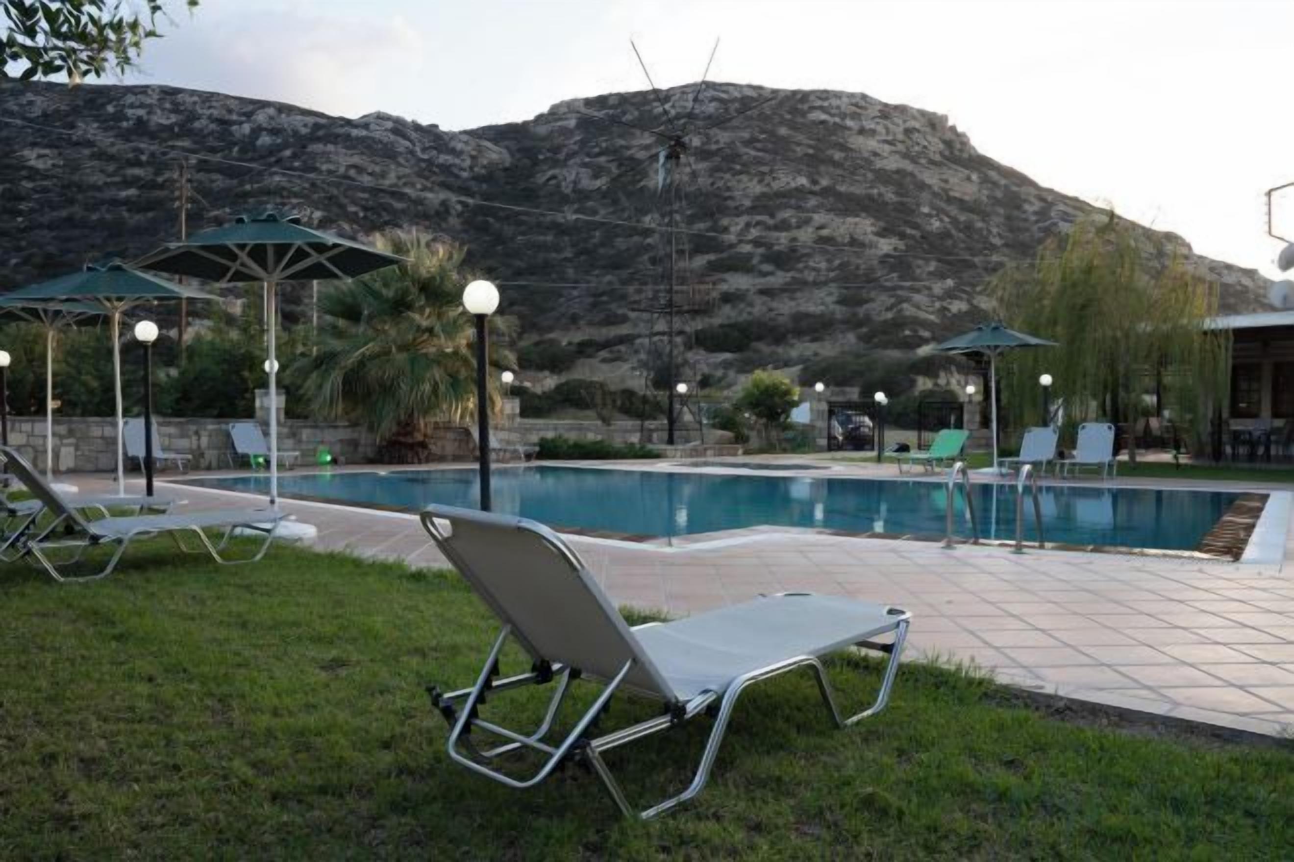 A pool area with lounge chairs and umbrellas, surrounded by a mountainous landscape.