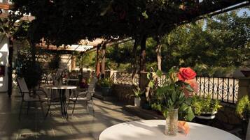 An outdoor patio with tables and chairs, surrounded by greenery and a pergola.