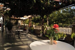 Un patio exterior con mesas y sillas, rodeado de vegetación y una pérgola.