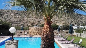 A pool with a stone wall, lounge chairs, and a palm tree. - Matala Dimitris Resort (Matala)