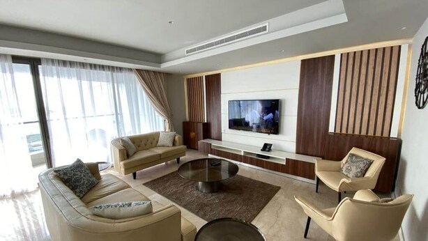 Ein modernes Wohnzimmer mit einer Couch, Sesseln, einem Couchtisch und einem an der Wand befestigten Fernseher.