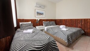 A hotel room with two beds, each with zebra-striped bedding, a white bedside table, a wall-mounted air conditioner, and a framed picture on the wall. - ONES PANSİYON (Kumluca)