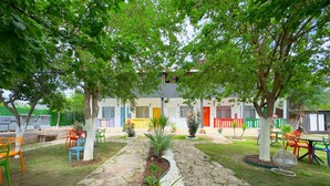 A courtyard with a stone pathway, colorful chairs, and potted plants. - ONES PANSİYON (Kumluca)