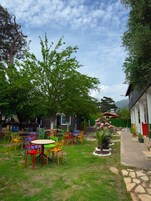 Un patio con mesas al aire libre, un pequeño jardín y un edificio de techo rojo.
