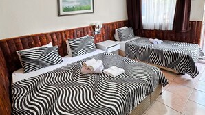 A hotel room with two beds, each with a zebra-striped bedspread, a framed picture on the wall, an air conditioning unit, and a window with curtains. - ONES PANSİYON (Kumluca)