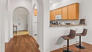 A modern kitchen with wooden cabinets, a microwave, and two bar stools. - Bella Notte At Caribe Cove (Kissimmee)