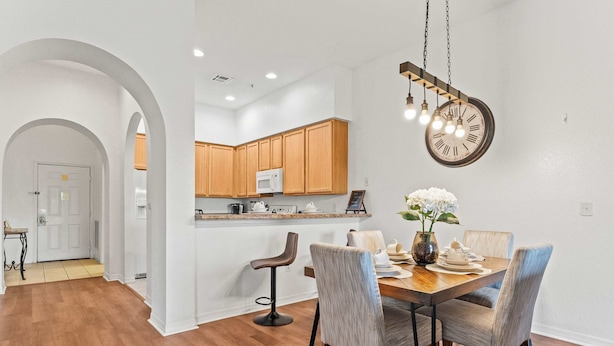 A modern kitchen with wooden cabinets, a microwave, and a dining area with a wooden table and chairs. - Bella Notte At Caribe Cove (Kissimmee)