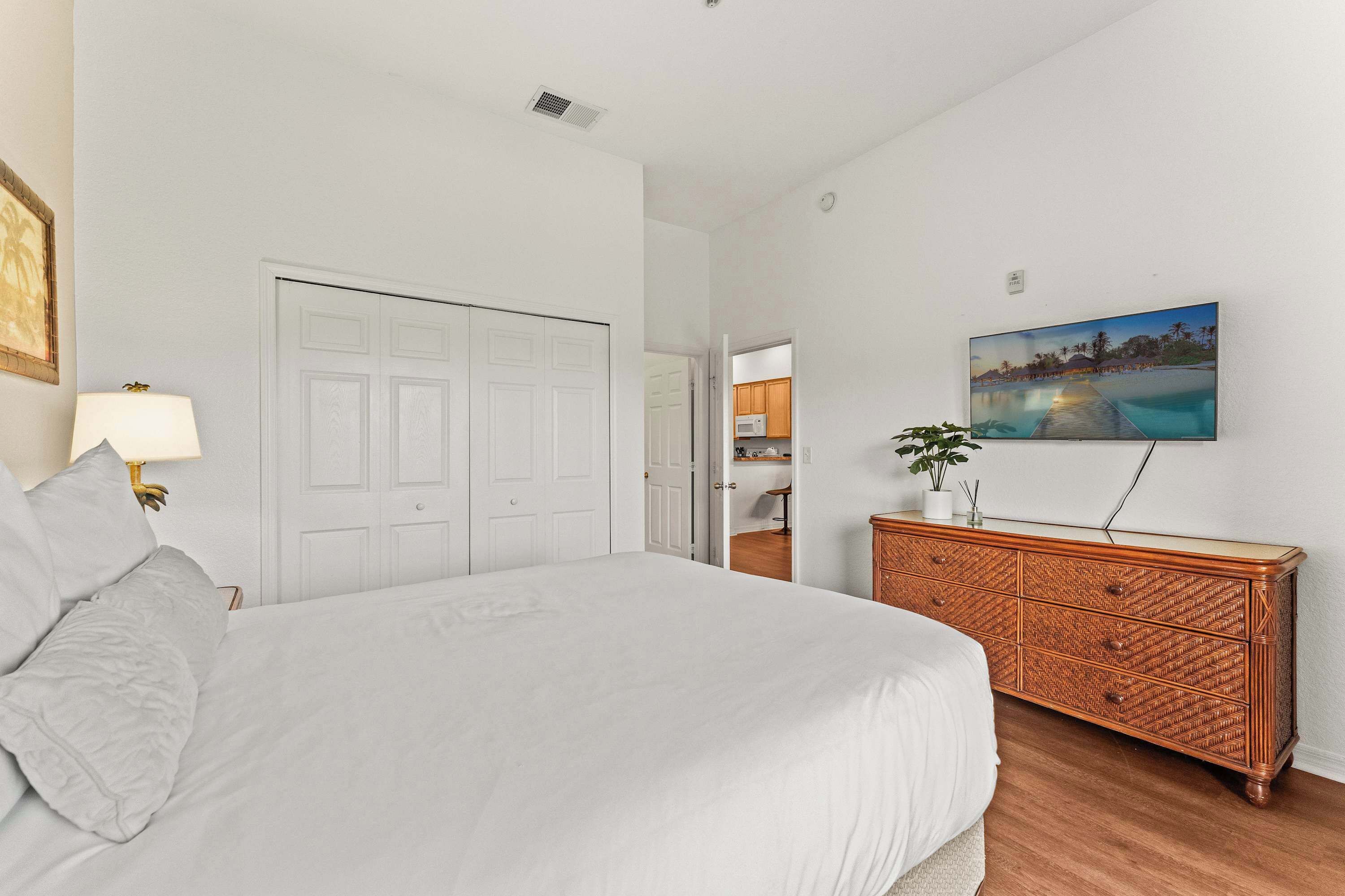 Une chambre à coucher avec un grand lit, une commode, un téléviseur fixé au mur et une porte donnant sur une salle de bain.