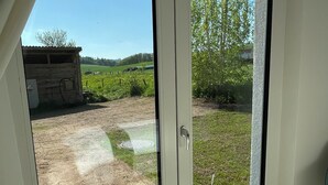 A room with a sliding glass door leading to an outdoor area with a dirt path, a wooden structure, and a grassy field. - Vacation home Wiesenblick (Spangenberg)