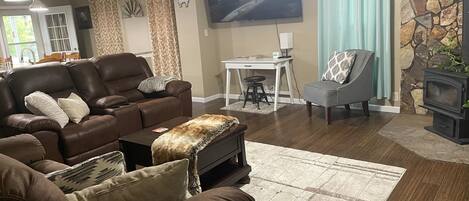 A living room with a brown leather sofa, a gray armchair, a stone fireplace, and a flat-screen TV mounted on the wall.