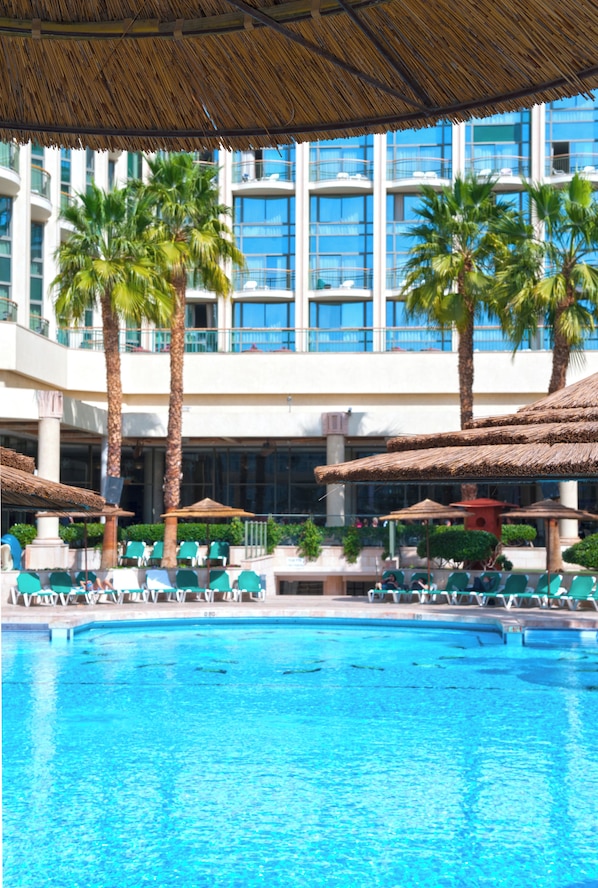 Una piscina con sillas de descanso y palmeras, rodeada por un edificio con balcones.